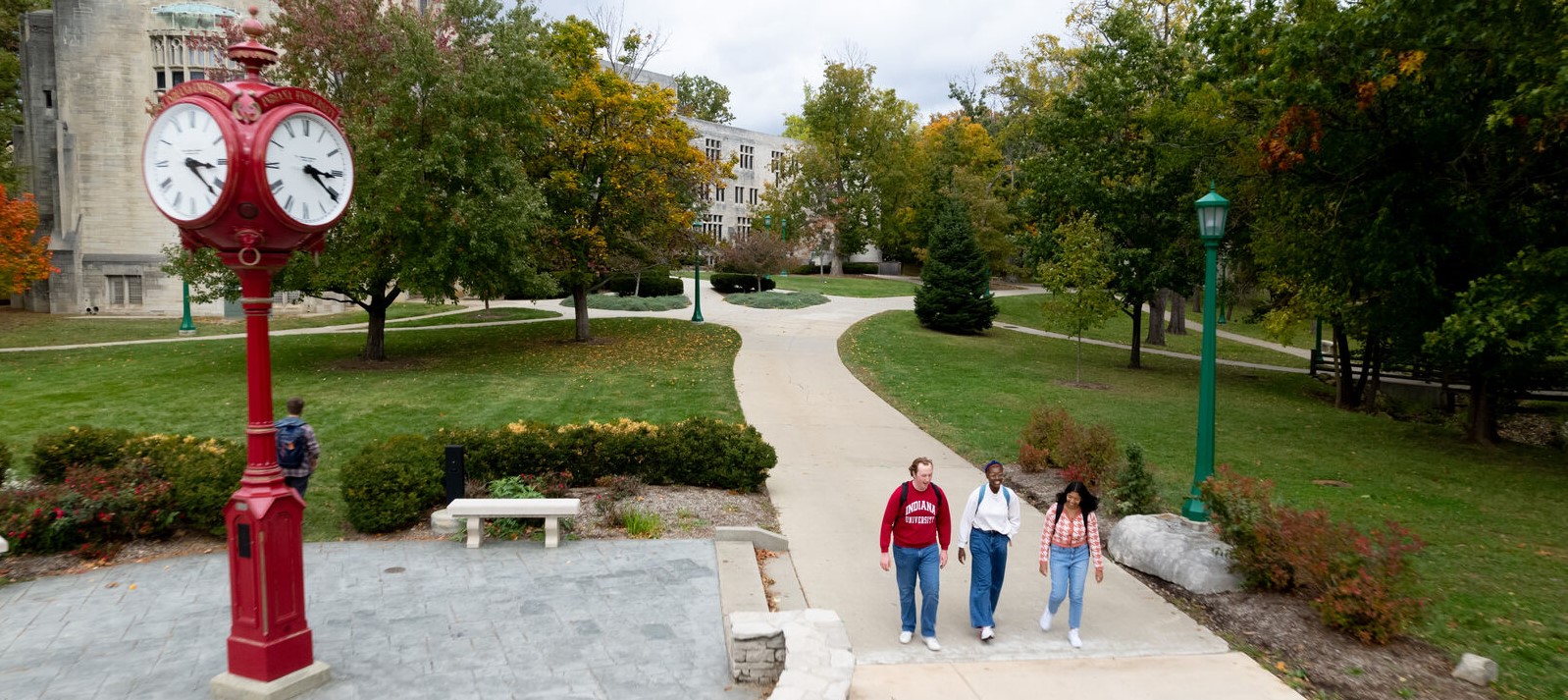 Three students walking on the IU Bloomington campus near a red clock.